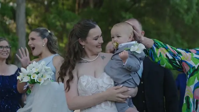 Wedding film still: bride laughing with a baby during the speeches