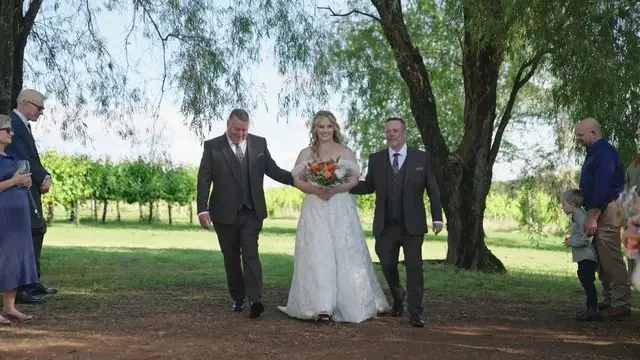 Wedding film still: bride walking the aisle under gum trees