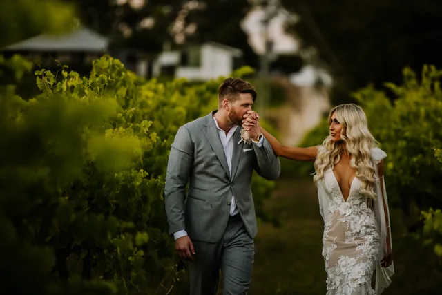 Groom kissing his bride's hand beside the vines