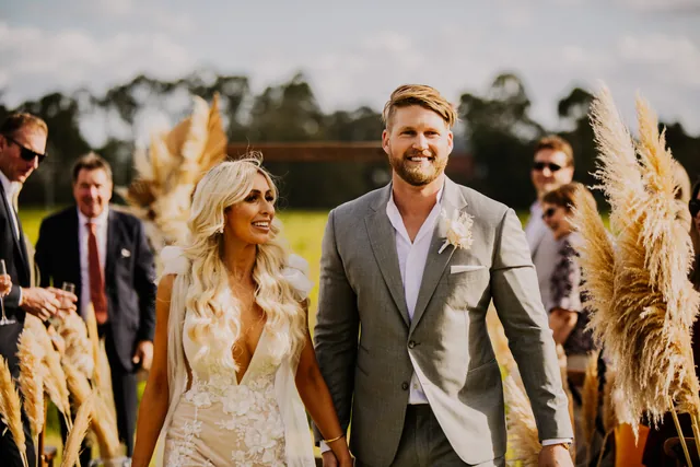 Bride and groom walking with their guests through the pampas grass