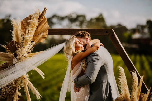 Couple embracing beneath a pampas grass ceremony arch