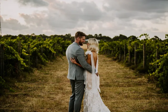 Bride and groom embracing between the vine rows at Riverbank Estate