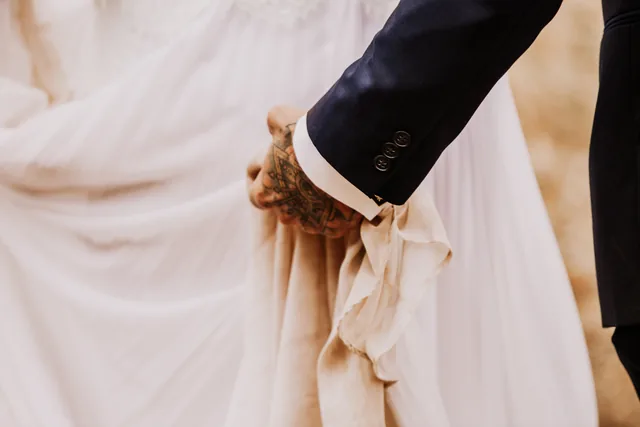 Detail of the bride's dress and the groom's tattooed hand
