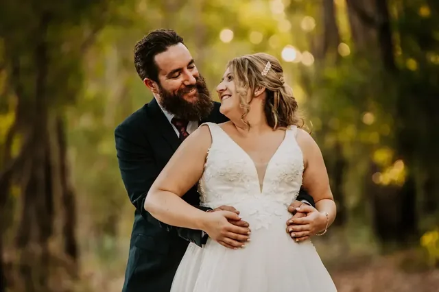 Groom holding his bride, both laughing, in the bush