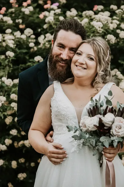 Melissa and Gavin close together in front of white roses