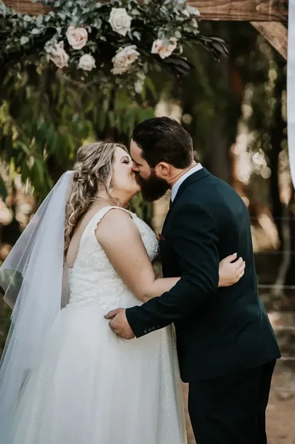 Bride and groom kissing beneath the floral arch
