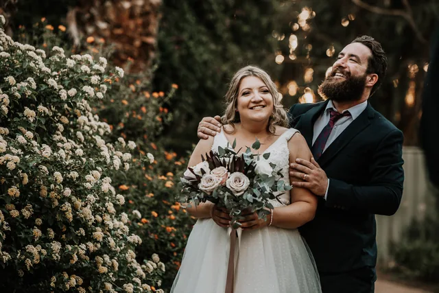 Bride and groom in front of the flowering hedge at golden hour