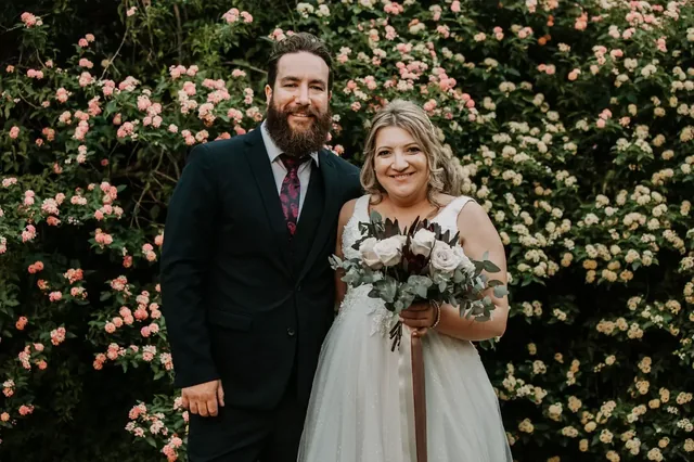 Bride and groom in front of a flowering rose hedge