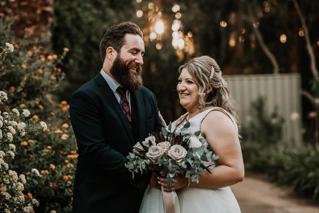 Bride and groom laughing together, bouquet in hand