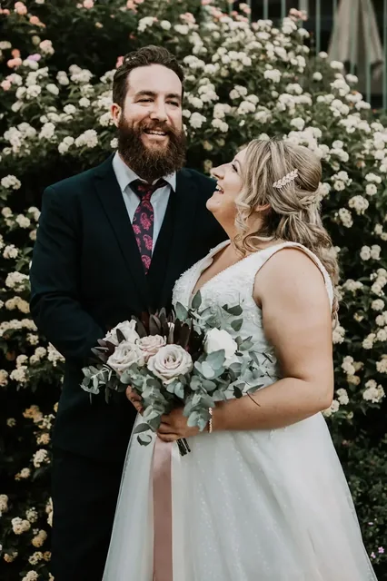 Bride holding her bouquet beside her groom in the roses