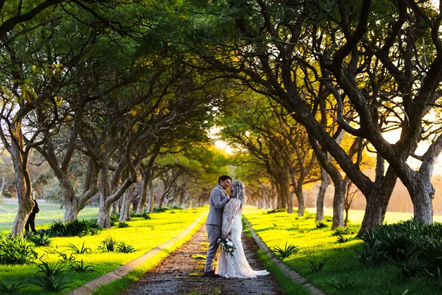 Two brides kissing on the path beneath the tree avenue at Quarry Farm