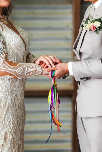 The brides’ hands bound with rainbow ribbon during the handfasting