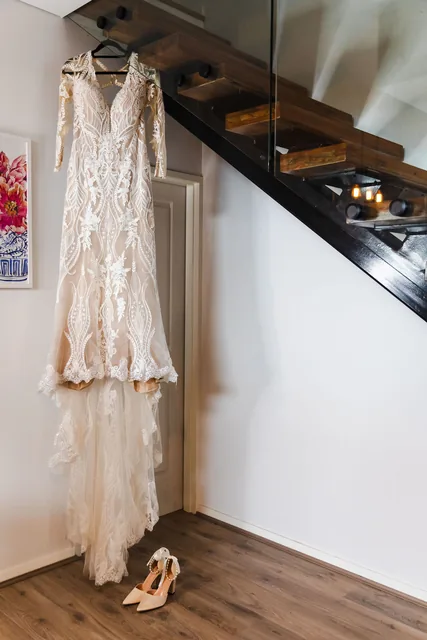 The lace gown hanging by the stairs, shoes waiting beneath
