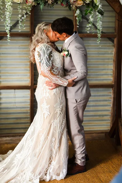 Two brides kissing in the shed doorway, framed by greenery