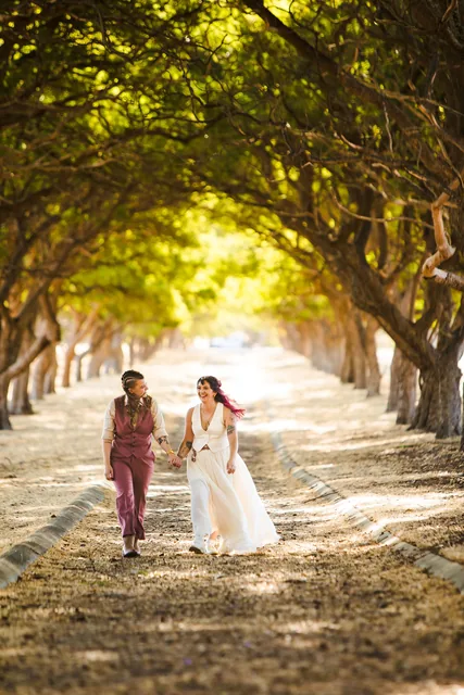 Two brides walking together in the dappled light of the tree avenue