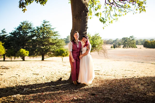 Two brides beneath a great old tree with the paddocks behind