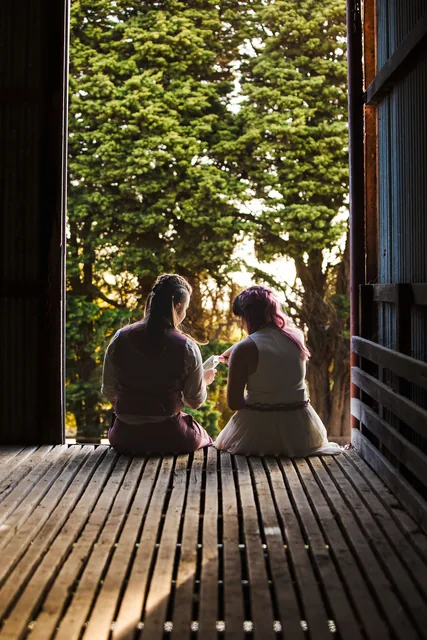 The two brides sitting together in the shade, looking out at the trees