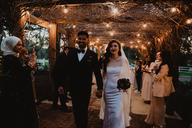 The couple walking the lit vine arbour as guests watch