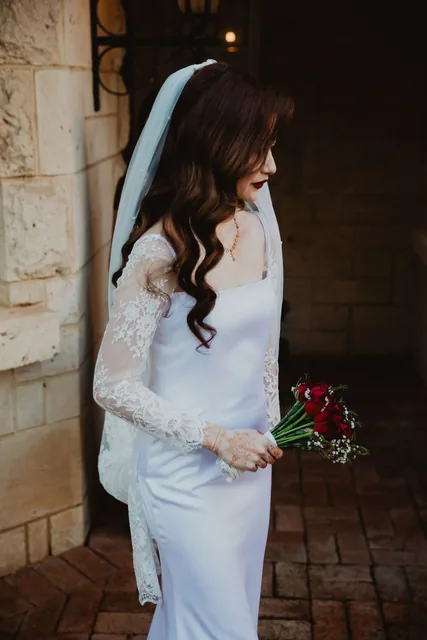 The bride in white against the limestone wall with a red bouquet
