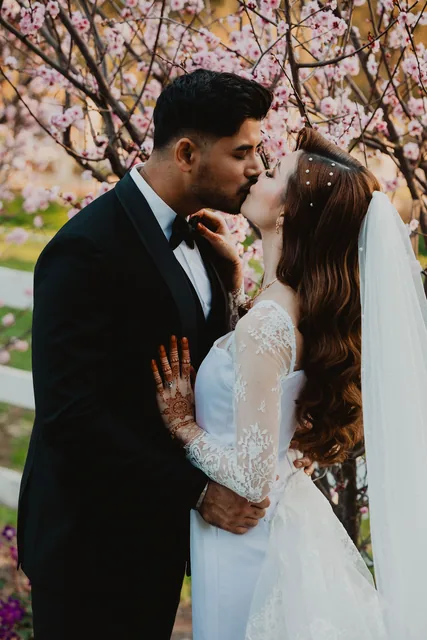 The groom kissing his bride beneath the blossom tree