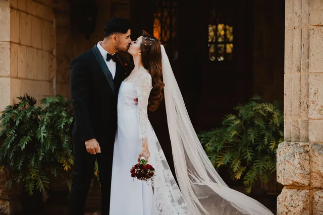 The couple kissing beneath the limestone colonnade, the veil trailing behind