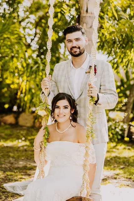 Groom pushing his bride on a rope swing beneath the trees