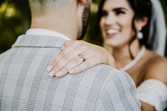 The bride's ring resting on her groom's shoulder as they embrace